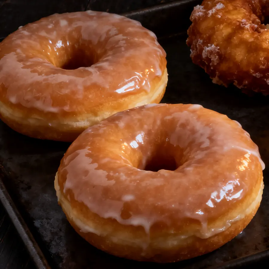 Two large glazed donuts on a dark baking tray
